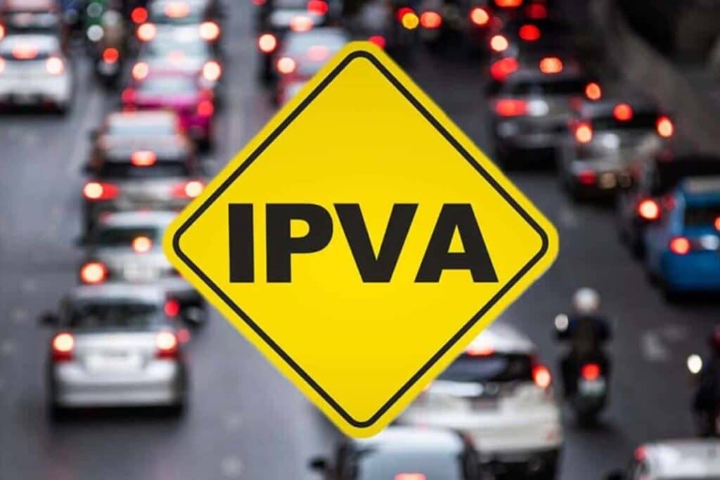 Placa amarela "IPVA" com trânsito ao fundo.